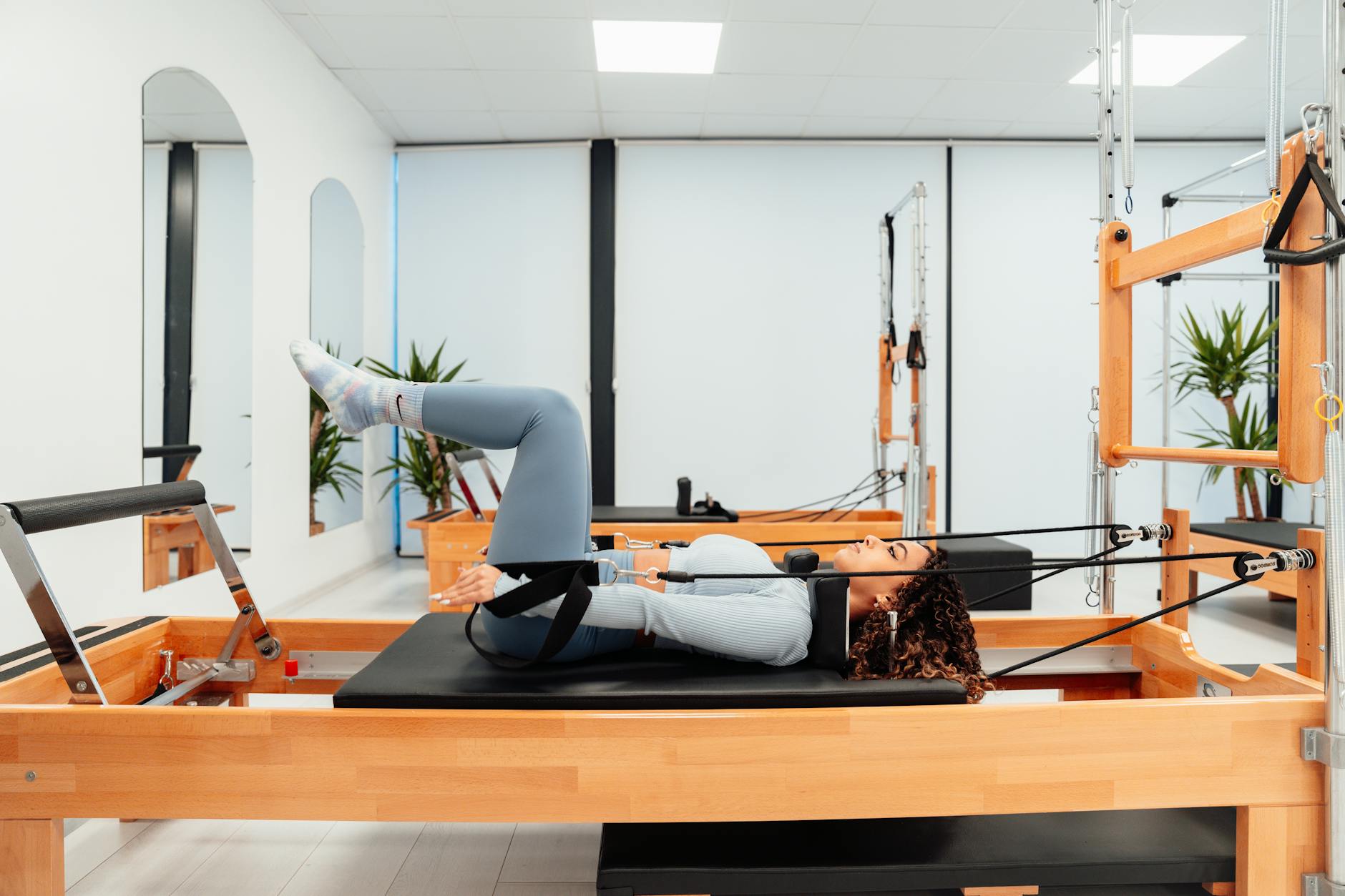 A woman performing fitness exercises on a Pilates reformer in a modern gym setting.