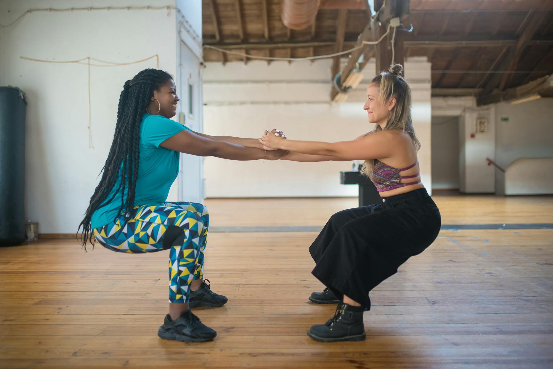 Two women doing partner squats in a bright studio, focusing on fitness and teamwork.