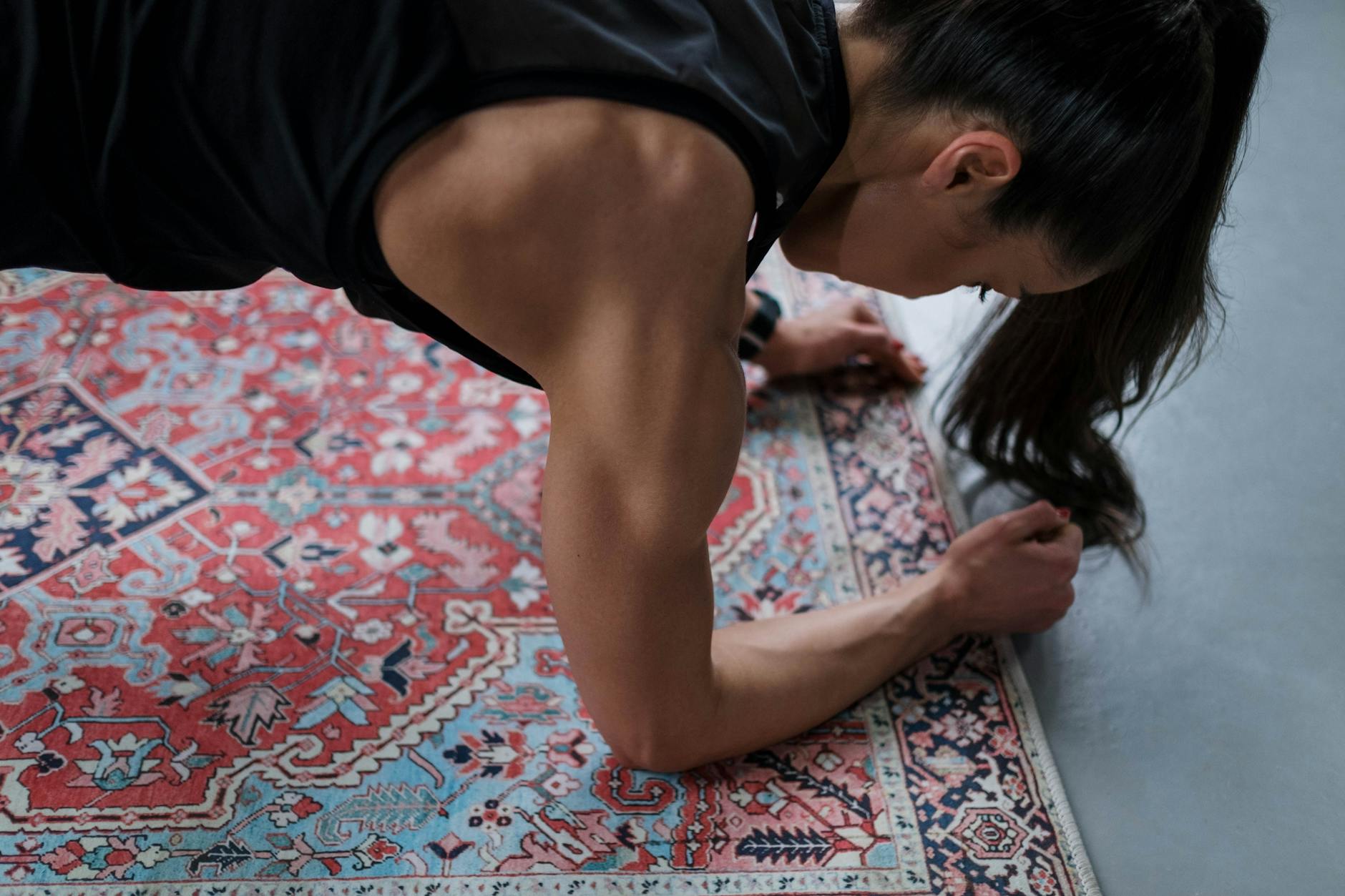Woman performing a plank exercise on a patterned rug, showcasing muscular strength and focus.